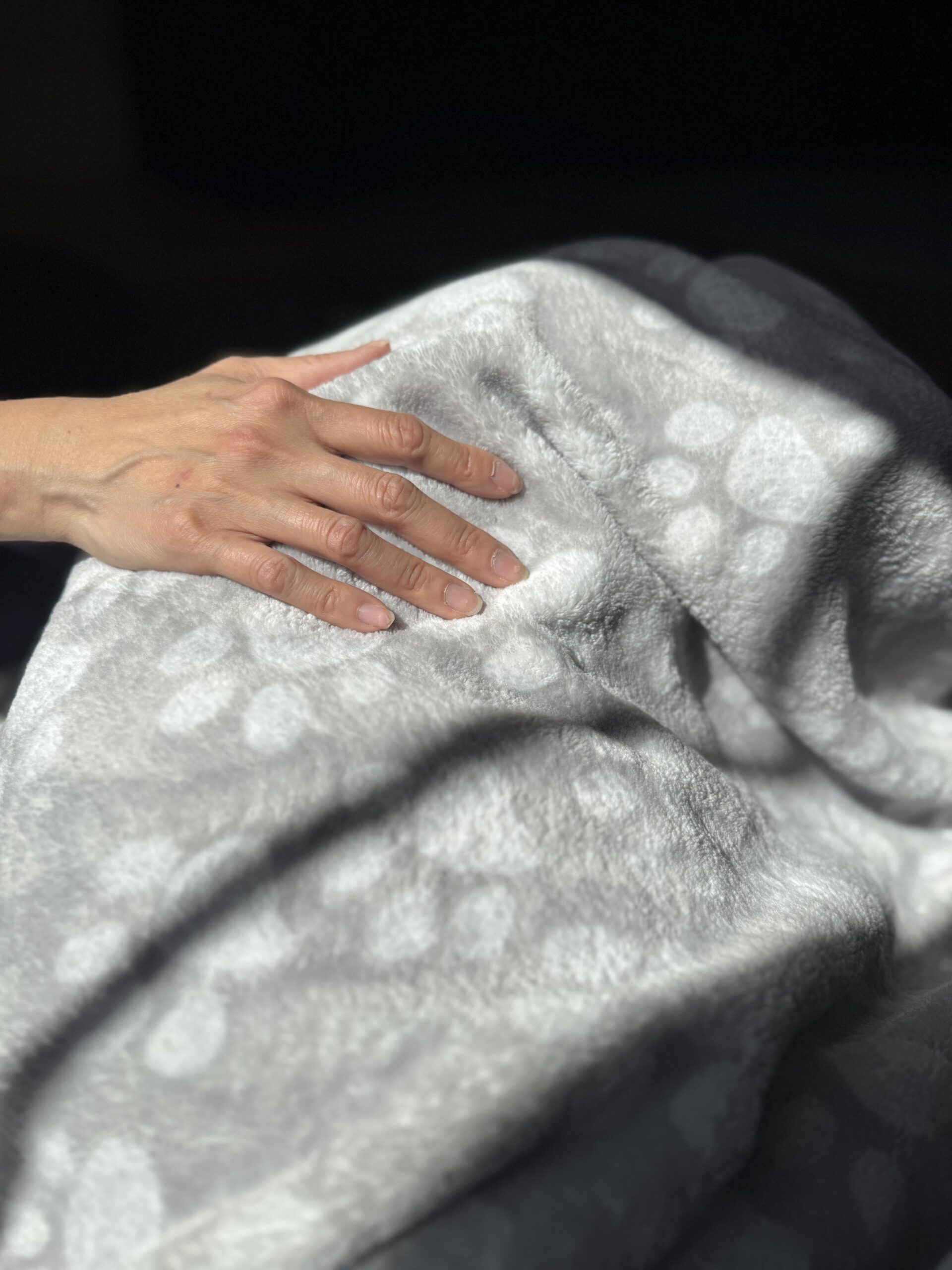 A person's hand gently rests on a blanket