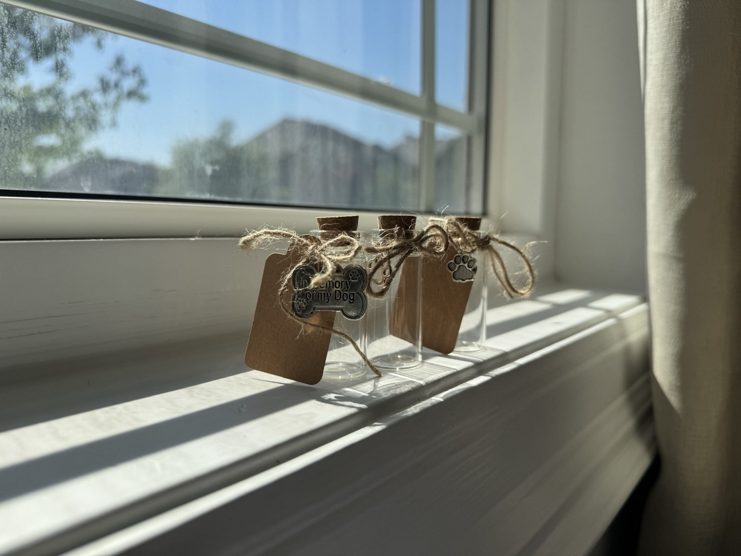 Three small glass keepsake vials with cork stoppers sit on a sunlit windowsill