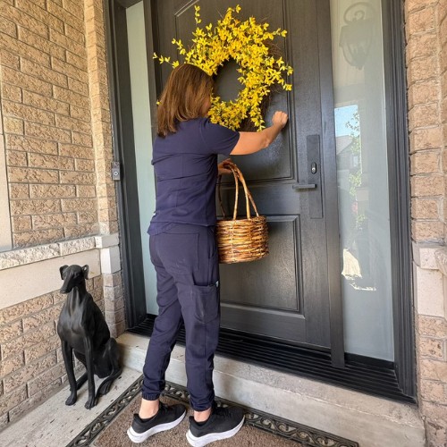 A woman standing at a front door holds a woven wicker basket